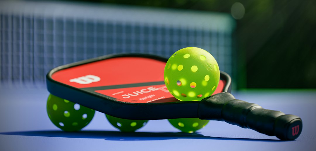 A red pickleball paddle and four neon yellow balls on a blue court