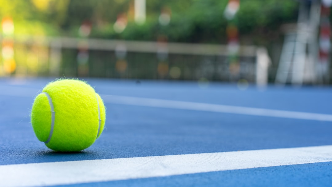 A bright yellow tennis ball rests on a blue court.