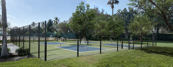 Outdoor pickleball courts surrounded by trees and grass.