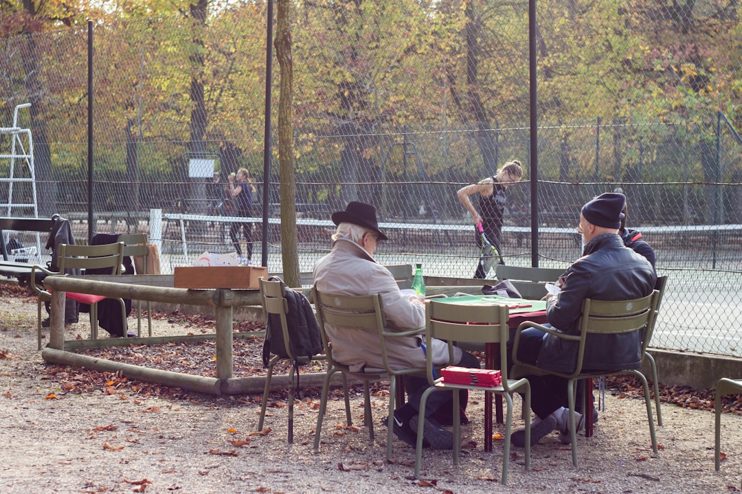 Two men watch a tennis match from outdoor chairs.