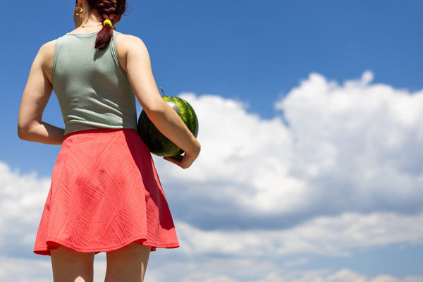 Woman in red skirt holding a watermelon under blue sky.