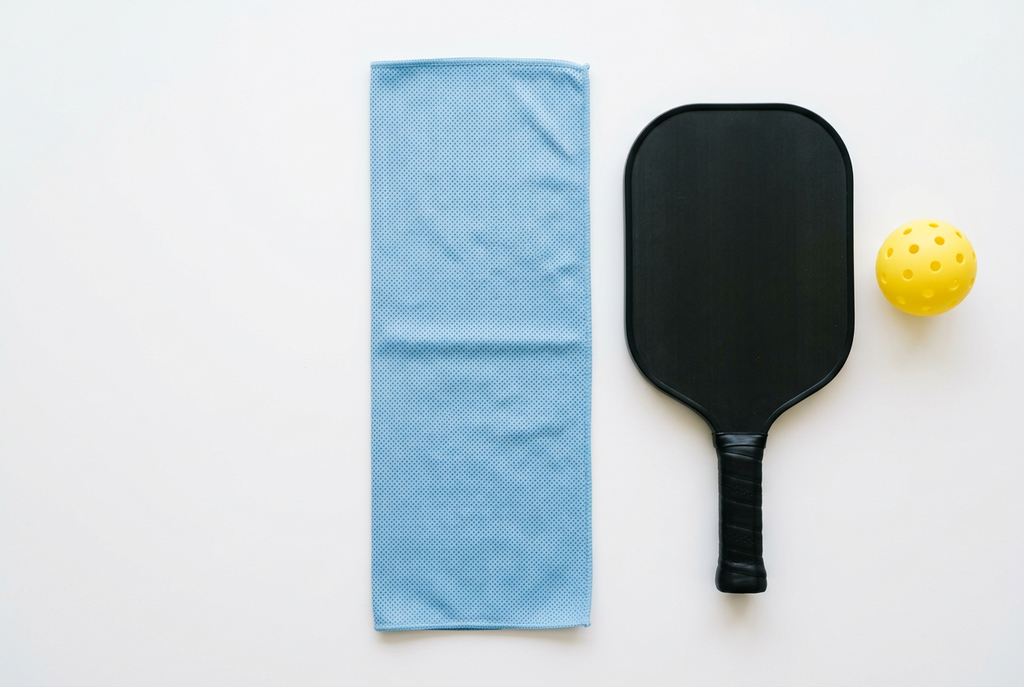 Cooling neck towel laid flat next to a pickleball paddle and ball to show its size